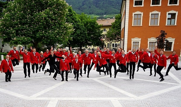 Der Chor des MGV Schlanders in roter Vereinstracht springt auf einem Platz in die Luft